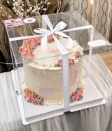Floral cake in a clear pickup box with a white ribbon
